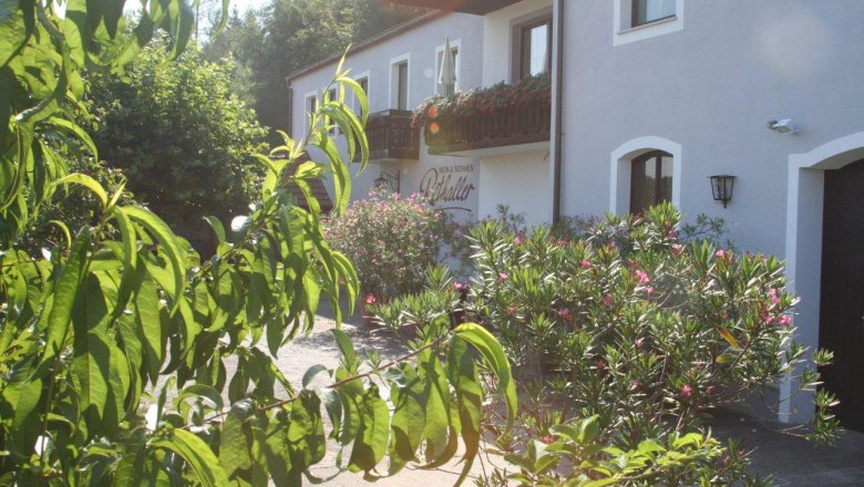 Exterior view detail, © Fam. Rethaller Exterior view of a building with a balcony and flowering shrubs in the foreground.