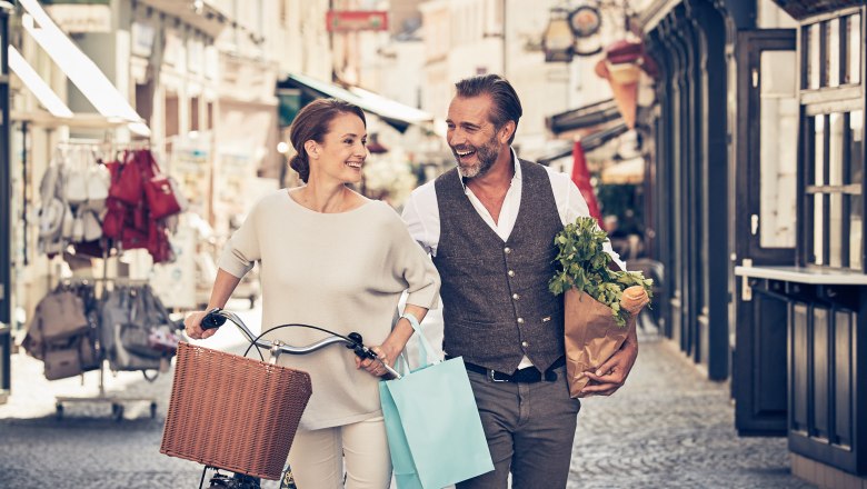 Old town of Krems, © Andreas Hofer A smiling couple strolls through an old town with shopping bags and a bicycle.