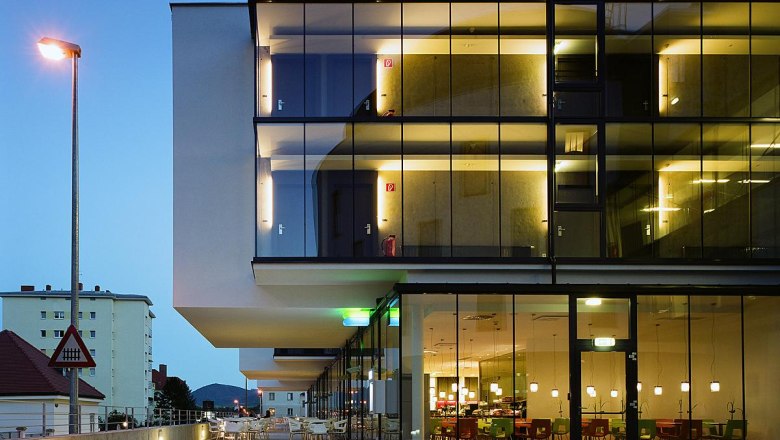 arte Hotel, © arte Hotel Modern hotel building with glass façade at dusk, illuminated interiors visible.