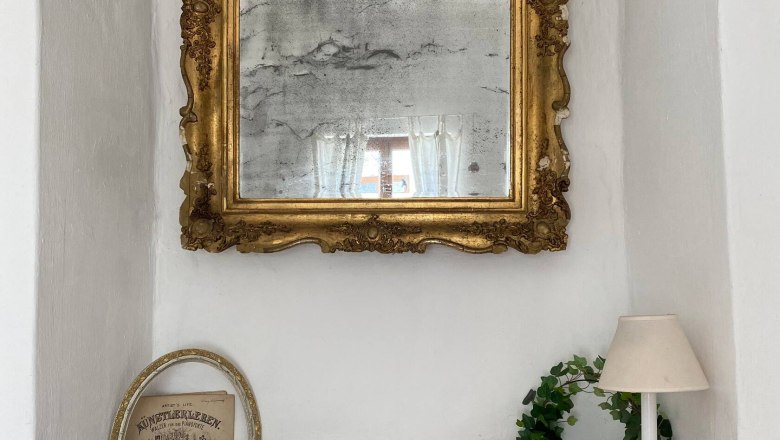 Fensterdeko, © Familie Stagard Ein antiker Spiegel mit goldener Verzierung über einer Fensterbank mit Deko.