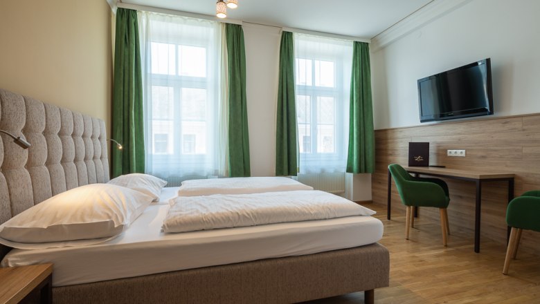 Hotel Unter den Linden 206, © Hotel Unter den Linden Hotel room with double bed, green curtains, desk, chair and wall-mounted TV.
