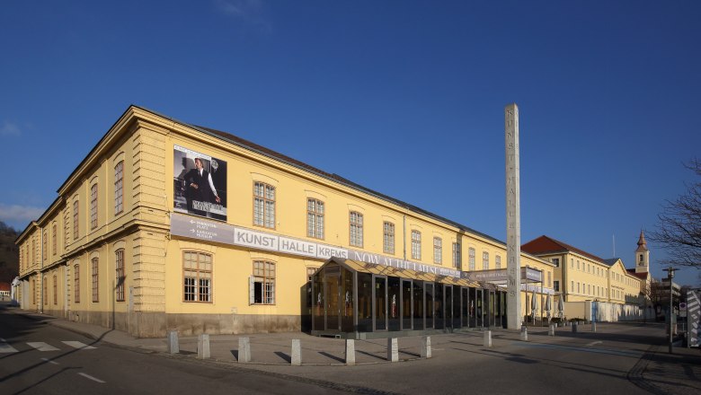 Krems Art Gallery, © Christian Redtenbacher Exterior view of the Kunsthalle Krems, a yellow building with large windows and a poster on the façade.