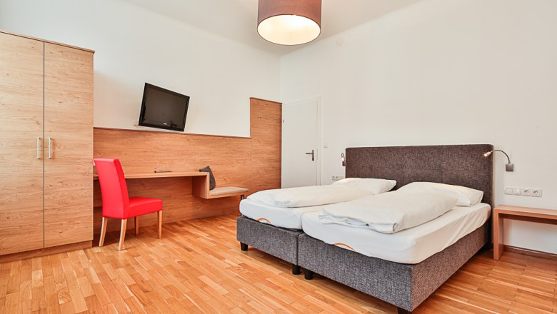 Hotel Unter den Linden Room 103, © Hotel Unter den Linden Hotel room with double bed, red chair, desk and TV.
