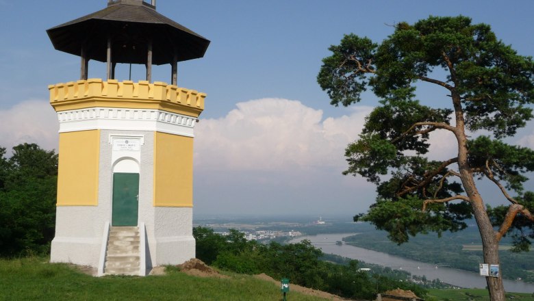 Danube Observatory at Egelsee, © www.oetk.at A yellow observation tower with a dark roof stands on a hill with a view of the Danube river and a town in the background.