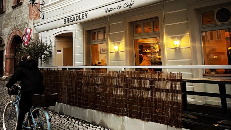 BREADLEY BISTRO, © Marek Safranek Außenansicht eines Cafés mit einem Radfahrer auf Kopfsteinpflaster.