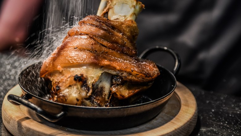 Hofbräu am Steinertor, © Extra Krems Knusprige Schweinshaxe in einer Pfanne auf einem Holzbrett, mit Salz bestreut.