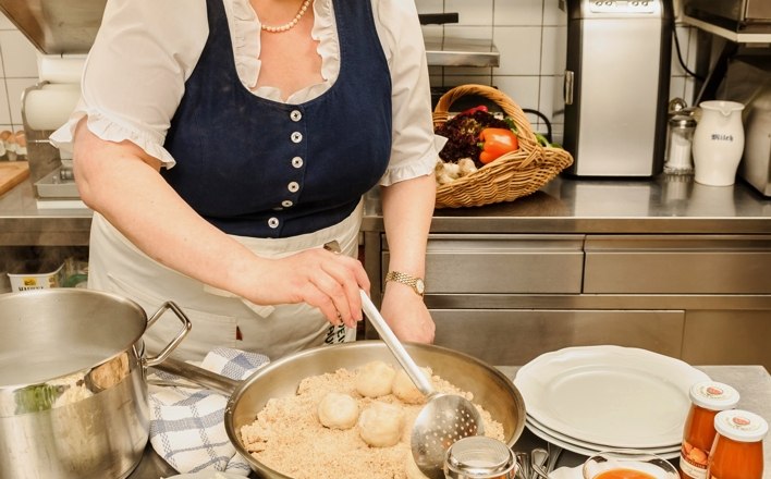 Ilse kocht Regionales aus besten Zutaten, © Rita Newman Frau in traditioneller Kleidung kocht in einer Küche mit regionalen Zutaten.