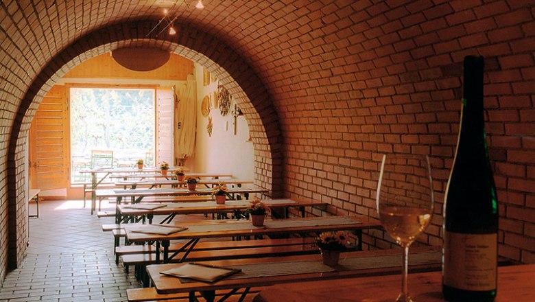keller-judmann02, © Anton Judmann Weinkeller mit Ziegelgewölbe, Holztischen und Weinflasche.