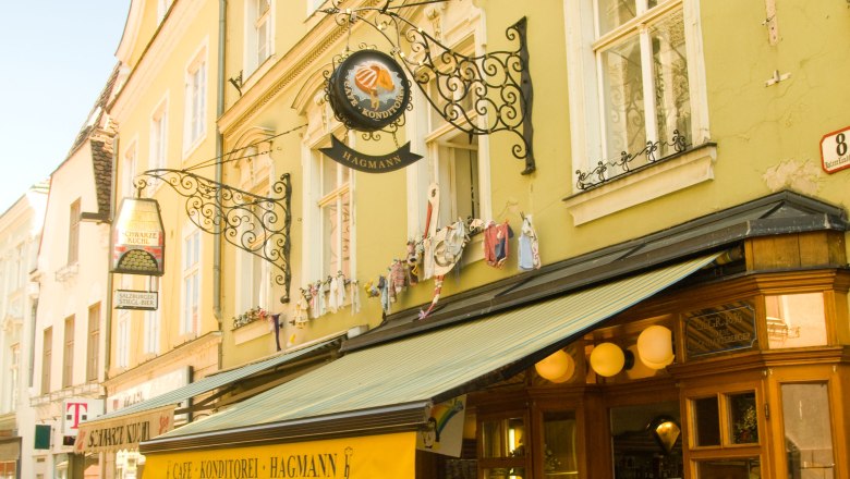 Konditorei Hagmann, © Konditorei Hagmann Außenansicht der Konditorei Hagmann mit gelbem Vordach und Straßencafé.