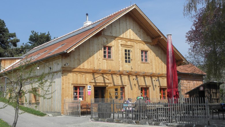 Schwarzalm Inn, Krems, © Gasthaus Schwarzalm Krems Wooden building with red roof and fence, sunny day.