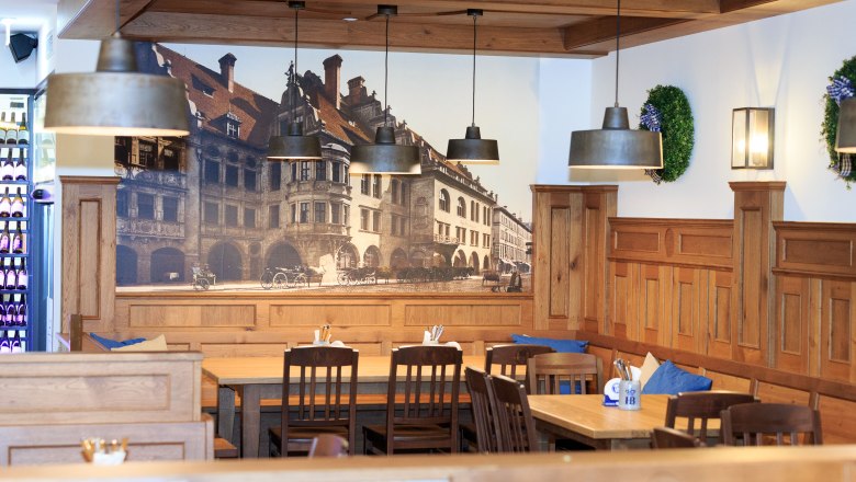 Hofbräu, © Ewald Rauscher Innenansicht eines traditionellen bayerischen Restaurants mit Holzmöbeln und Wandbild des Hofbräuhauses.