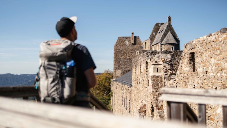 Auf der Burgruine Aggstein, © NÖW Franziska Consolati Ein Wanderer mit Rucksack betrachtet die Burgruine Aggstein an einem sonnigen Tag.