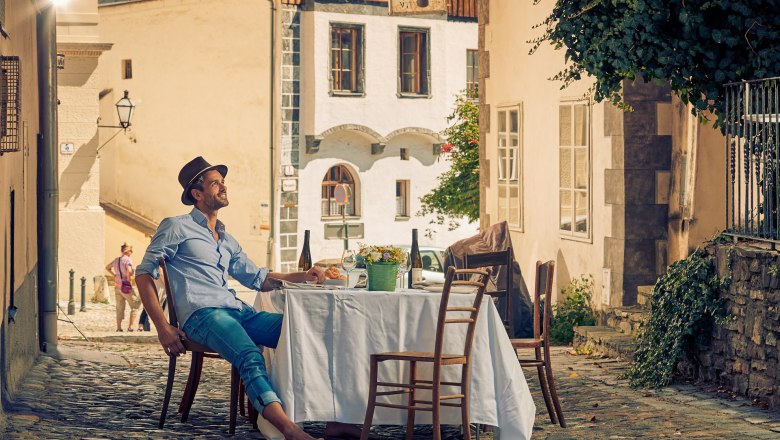 Old town of Krems, © Andreas Hofer Man sitting at a table in a cobbled alleyway in the old town of Krems.