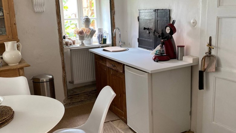 Küchenbereich, © Familie Stagard Küchenbereich mit kleinem Tisch, Stuhl, Spüle und Kaffeemaschine. Fenster mit Dekoration und helle Wände.