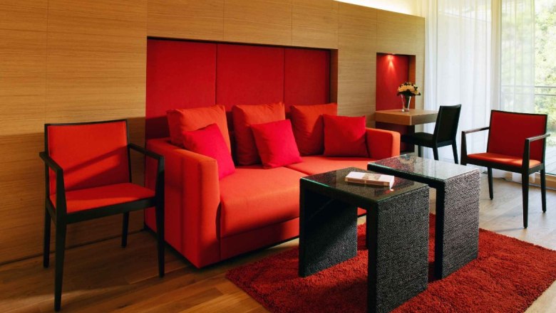 Vineyard suite, © Steigenberger Hotel and Spa Modern suite with red furniture and wooden walls.