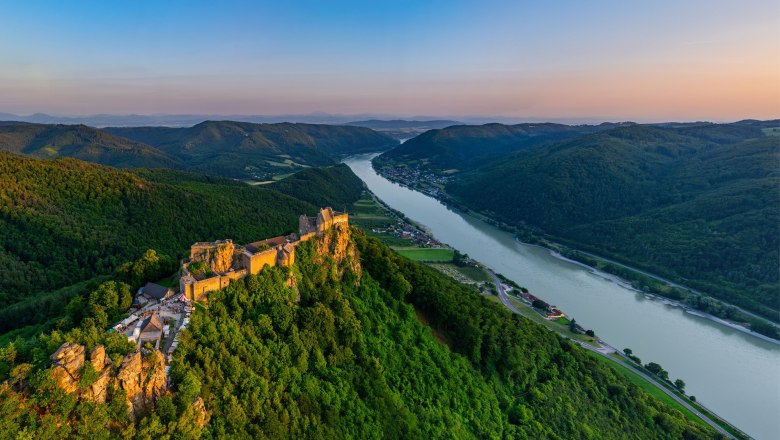Aggstein castle ruins, © Sebastina Wegerbauer Aerial view of the ruins of Aggstein Castle on the Danube, surrounded by green hills and forests at sunset.