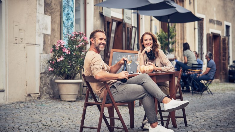 Old Town Krems, © Andreas Hofer A couple sits at a table in the old town of Krems, drinking wine and smiling. Other guests and historic buildings can be seen in the background.
