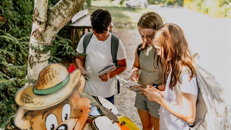 Kittenberg adventure gardens, © Matthias Streibel Three children with rucksacks reading cards next to a bear figure outdoors.
