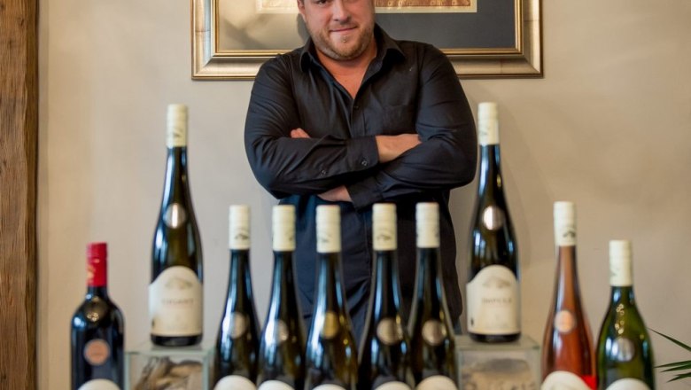 Toni Zöhrer, © Weingut Zöhrer Man standing behind a row of wine bottles on a table.