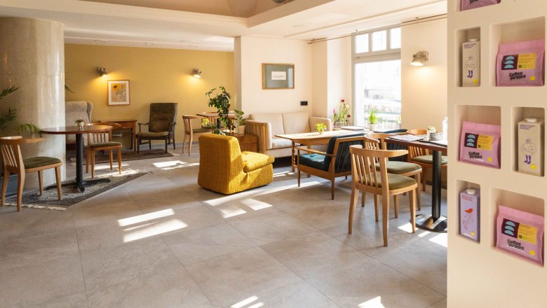 BREADLEY BISTRO, © Marie Grulich Innenansicht eines gemütlichen Cafés mit Holzmöbeln und Pflanzen.