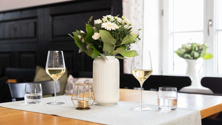 Ein Gläschen Wein im Gasthof genießen, © Werner Wachsmann Verlag Tisch mit zwei Weingläsern, Vase und Kerze