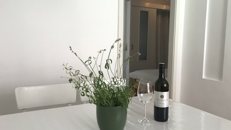 Bei einem Gläschen Wein entspannen, © Gästehaus Lurger Ein Tisch mit einer Weinflasche, einem Weinglas und einer Pflanze in einem Raum.