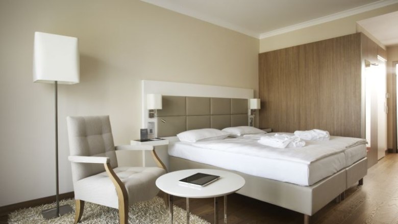 Standard double room, © Steigenberger Hotel and Spa Modern hotel room with double bed, armchair, table and floor lamp.