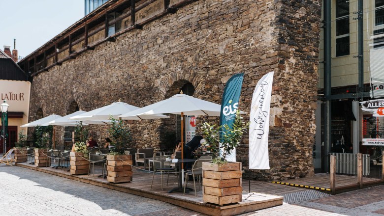 Café, Living Room, Outdoor Dining Area, © FMS Steinertor Gastronomie BetriebsgmbH Outdoor terrace of a café with parasols and plants in front of an old stone wall.