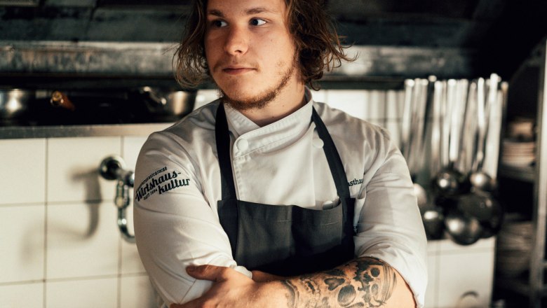 Laurent Amon hat das Zepter von Ulli Amon-Jell übernommen, © Niederösterreich Werbung/Julius Hirtzberger Junger Koch mit Tattoos in einer professionellen Küche, Arme verschränkt.