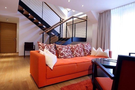 Senior Suite, © Steigenberger Hotel and Spa Modern suite with orange couch, decorative cushions and staircase in the background.