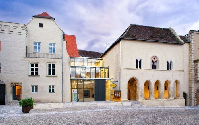 Gozzoburg, © Birgit Lechner Historisches Gebäude mit modernem Glaszwischenbau, Kopfsteinpflaster im Vordergrund.