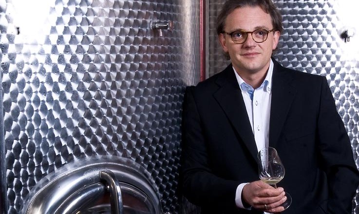 Johann Müllner, © Weingut Müllner Ein Mann in Anzug hält ein Weinglas vor einem großen Edelstahltank.