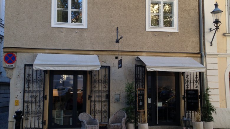 Woraczicky, © Woraczicky Small café with two wicker chairs in front of the door, beige façade, roof with dormer.