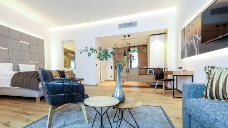 Outdoor-pool-view-from-top, © Klinglhuber Modern furnished hotel room with bed, armchairs, table and decoration.