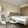Modern hotel room with double bed, armchair, table and floor lamp.