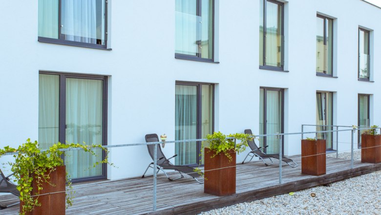 Modern terrace with sun loungers and plants in front of a building with large windows.