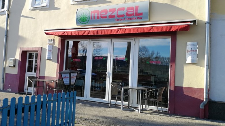 Außenansicht des Mezcal Restaurants mit roten Markisen und Sitzgelegenheiten.