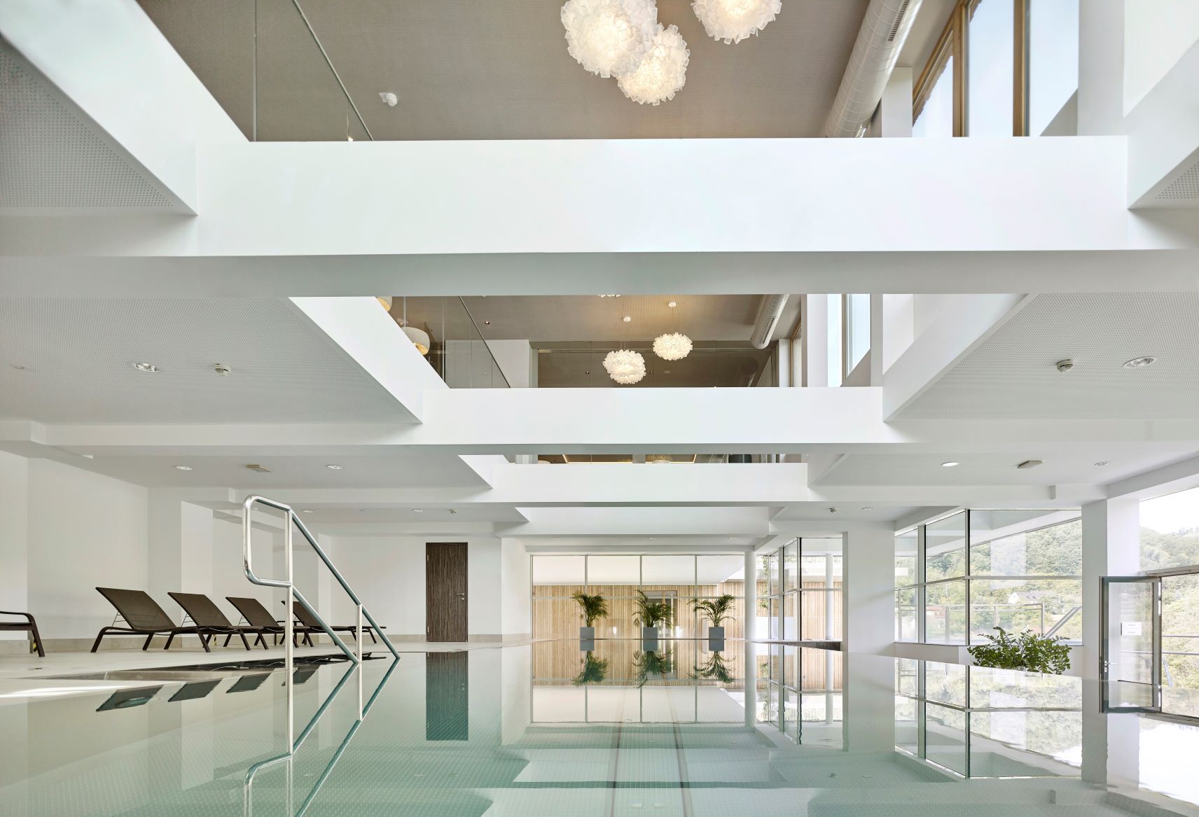 Indoorpool mit Liegestühlen und großen Fenstern.