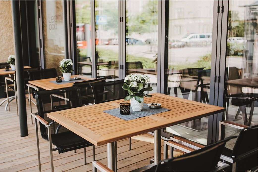 Terrasse einer Vinothek mit Holztischen, Stühlen und Blumen in Töpfen.