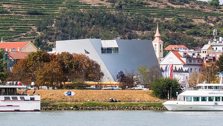 Moderne Architektur der Landesgalerie Niederösterreich am Flussufer mit umliegenden Gebäuden und Booten.