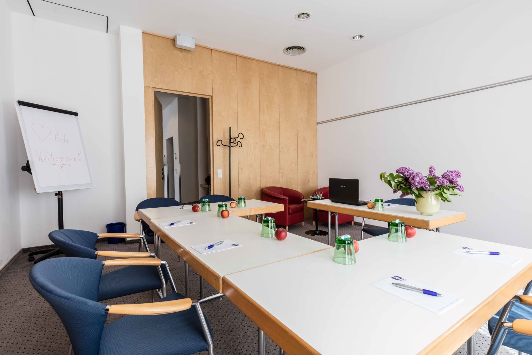 Konferenzraum mit Tischen, Stühlen, Flipchart und Blumen.