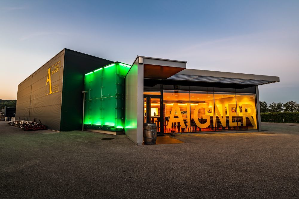 Modernes Weingut mit beleuchtetem Eingang und großem Schriftzug 'Aigner'.