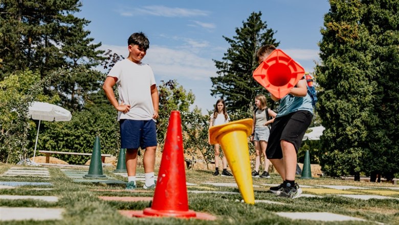 Children play outdoors with large colorful cones on a grass field.