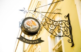 Metallschild 'Caf&eacute; Konditorei Hagmann' an einer gelben Hauswand.