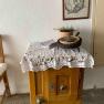 A small wooden table with a lace ceiling, plants and a framed picture on the wall.
