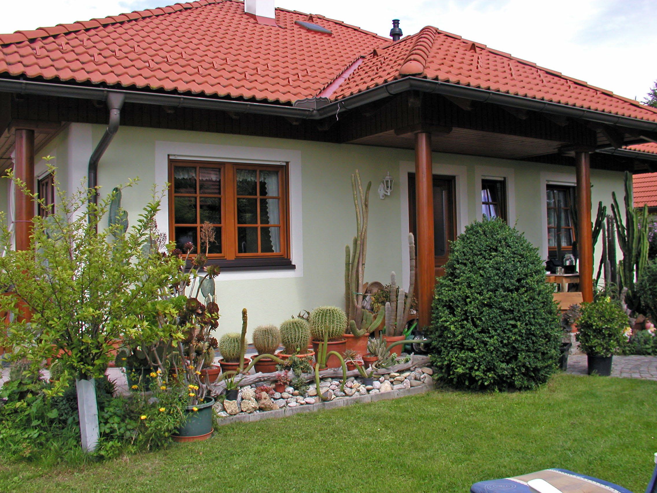 Ein Haus mit rotem Ziegeldach, umgeben von einem Garten mit Kakteen und Sträuchern.