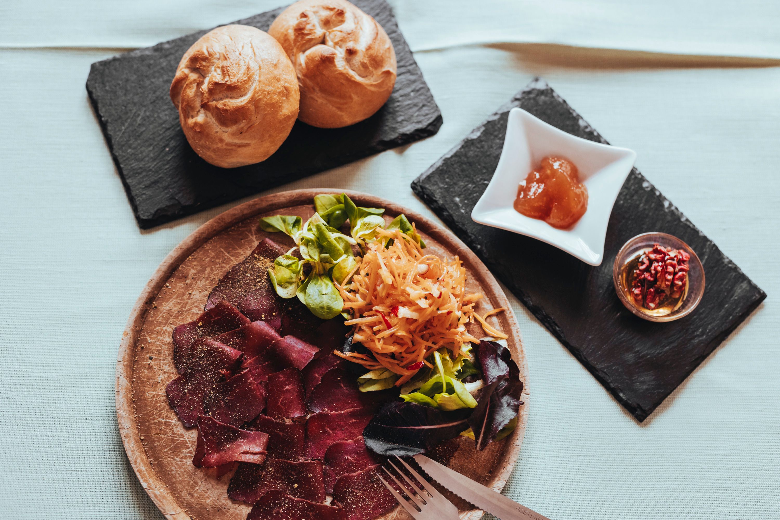Teller mit Schinken, Salat und Brötchen auf einem Tisch.
