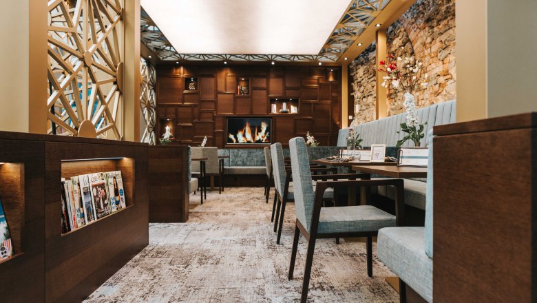 Innenansicht eines stilvollen Caf&eacute;s mit gem&uuml;tlichen Sitzgelegenheiten, Kamin und Zeitschriftenregal.