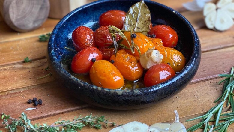 Eine Schale mit confierten Tomaten, Knoblauch und Kr&auml;utern auf einem Holztisch.