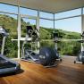 Fitness room with treadmill, cross trainer and exercise bike in front of large windows with a view of green hills.